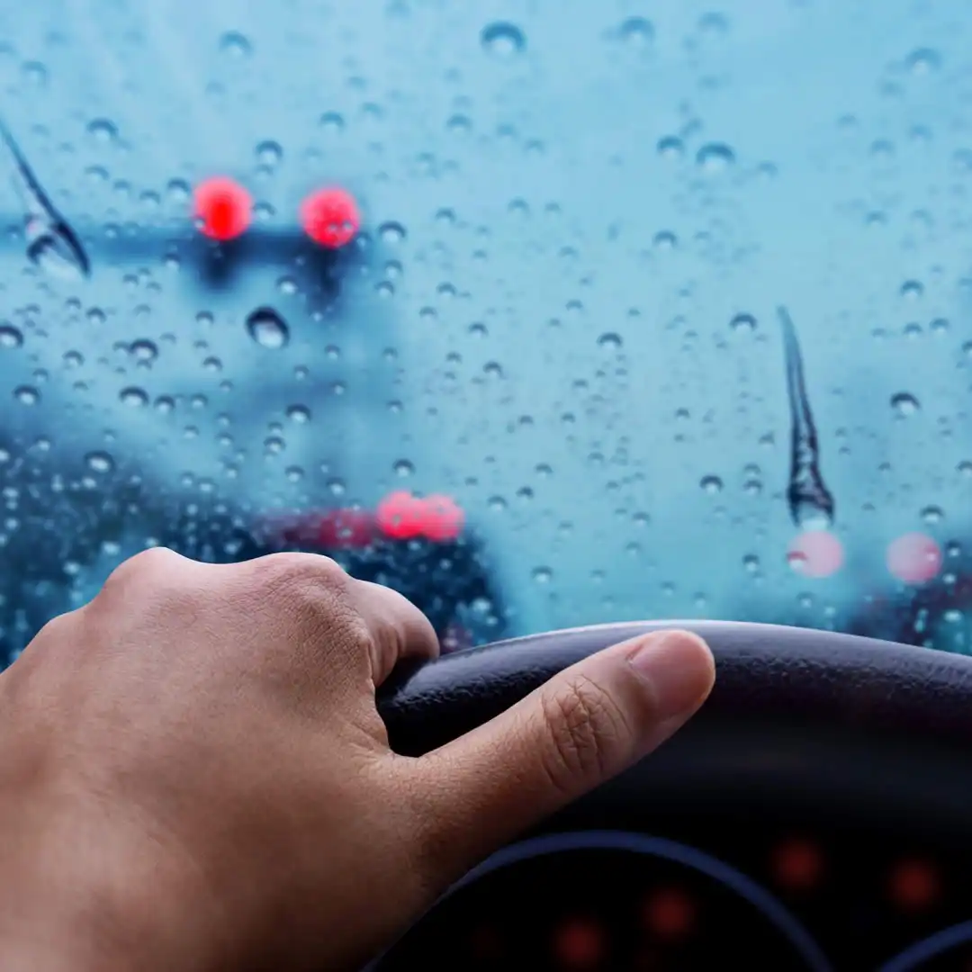 hand grips a steering wheel in front of a wet windshield